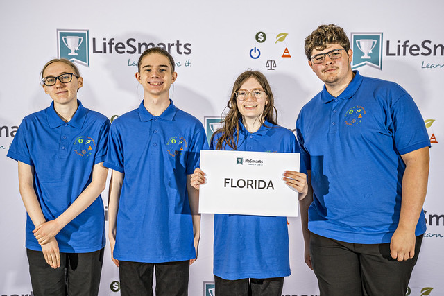Four young people in matching blue shirts, one holding a sign that says LifeSmarts Florida