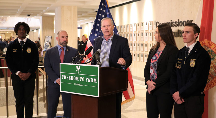 Commissioner Simpson speaking at a podium flanked by State Senator Jay Collins and State Representative Kaylee Tuck