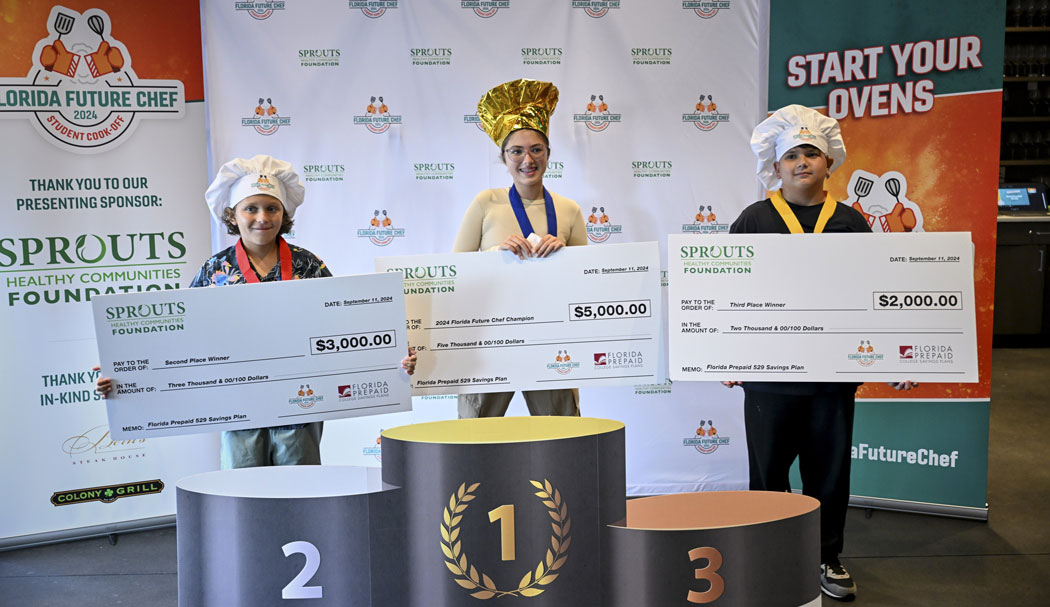 Three young people holding giant checks and wearing chef hats