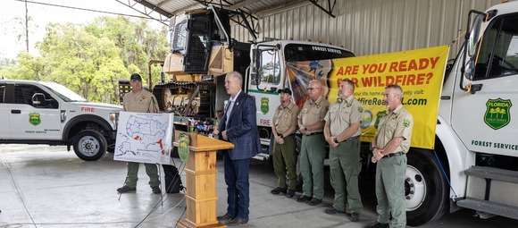 Commissioner Simpson speaking at a podium surrounded by forestry officials
