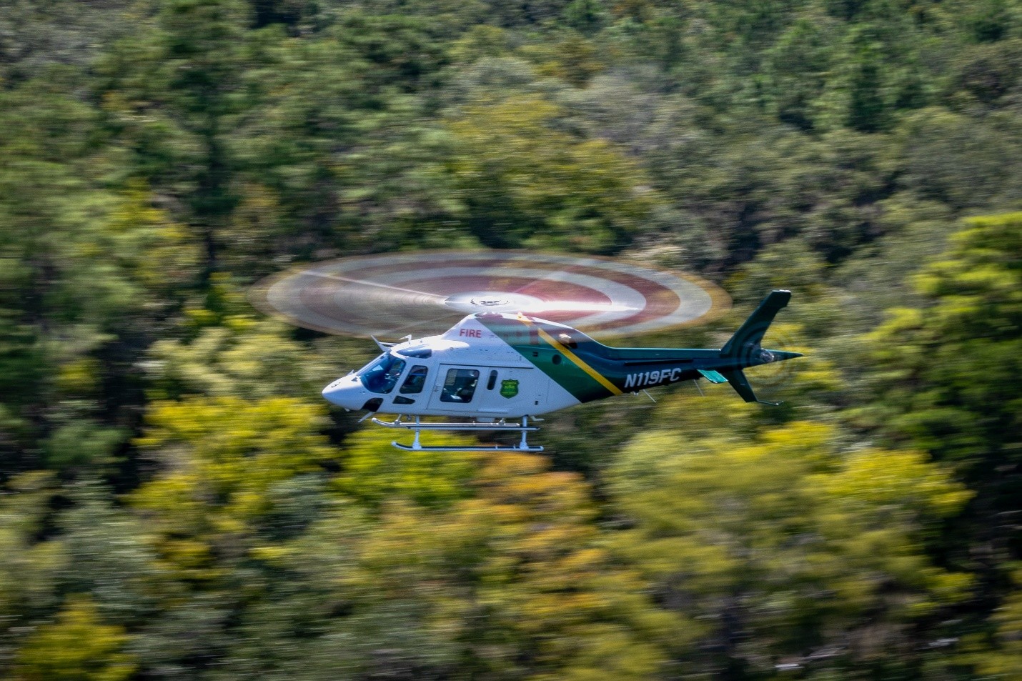 AW-119 helicopter flying over a forest